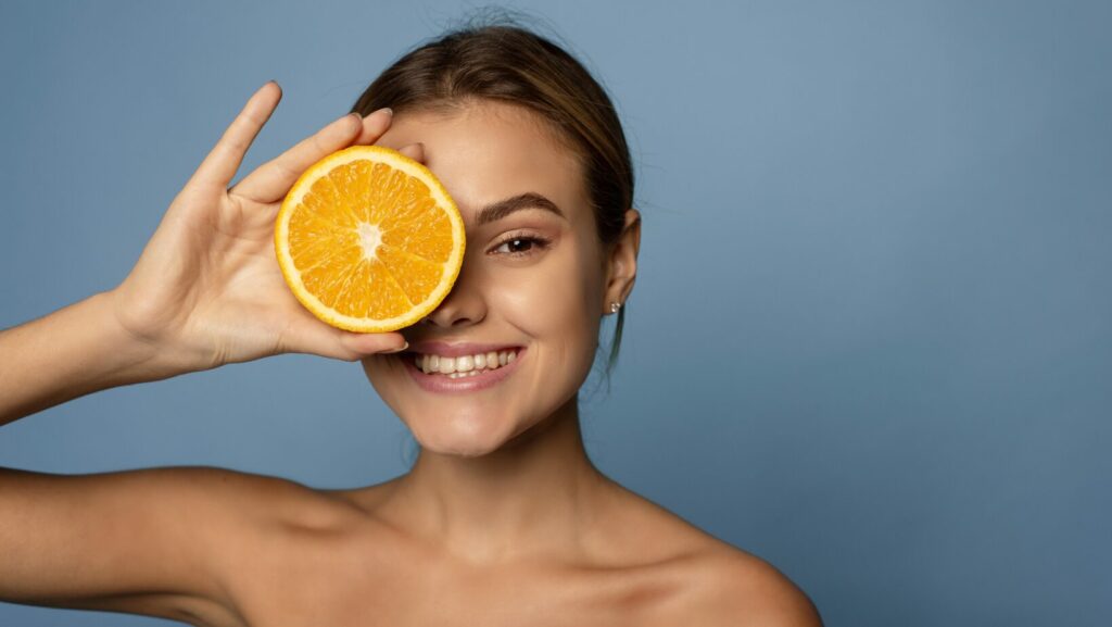 אישה מחזיקה בתפוז ליד העור כהמחשה לטימין C לעור הפנים